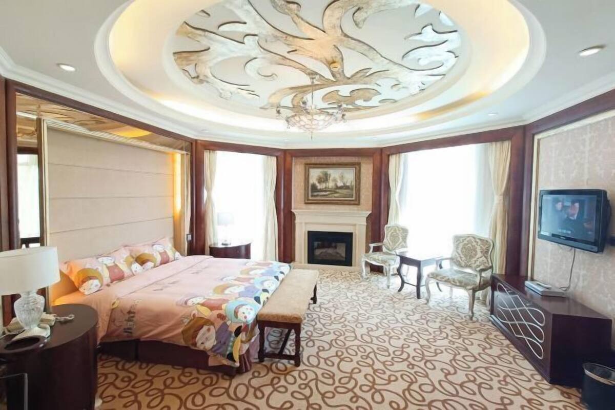 A hotel room with a large bed, a fireplace, a television, and a decorative ceiling.