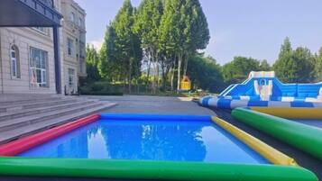 Ein Schwimmbecken mit aufblasbaren Rutschen und einem Gebäude im Hintergrund.