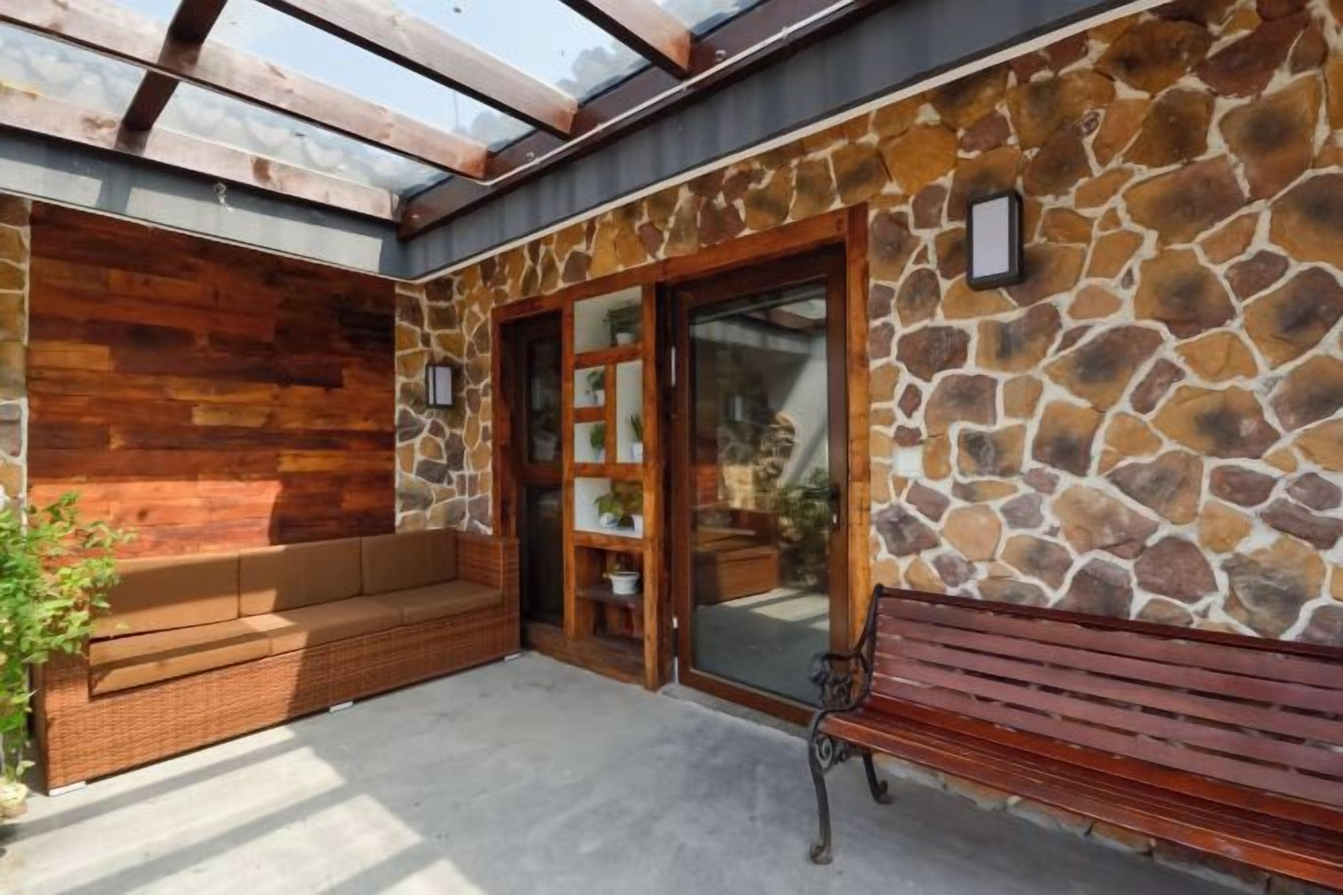 Un'area esterna coperta con un muro in pietra, una panca di legno e una porta in vetro che dà su una stanza.