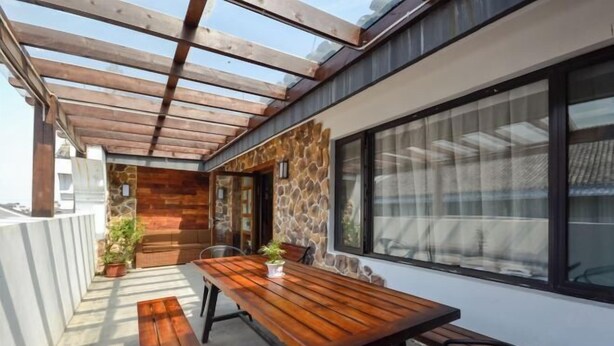 A covered outdoor patio with a wooden table and chairs, stone wall, and large windows. - Nanxun Kangyu Yashe Inn (Huzhou)