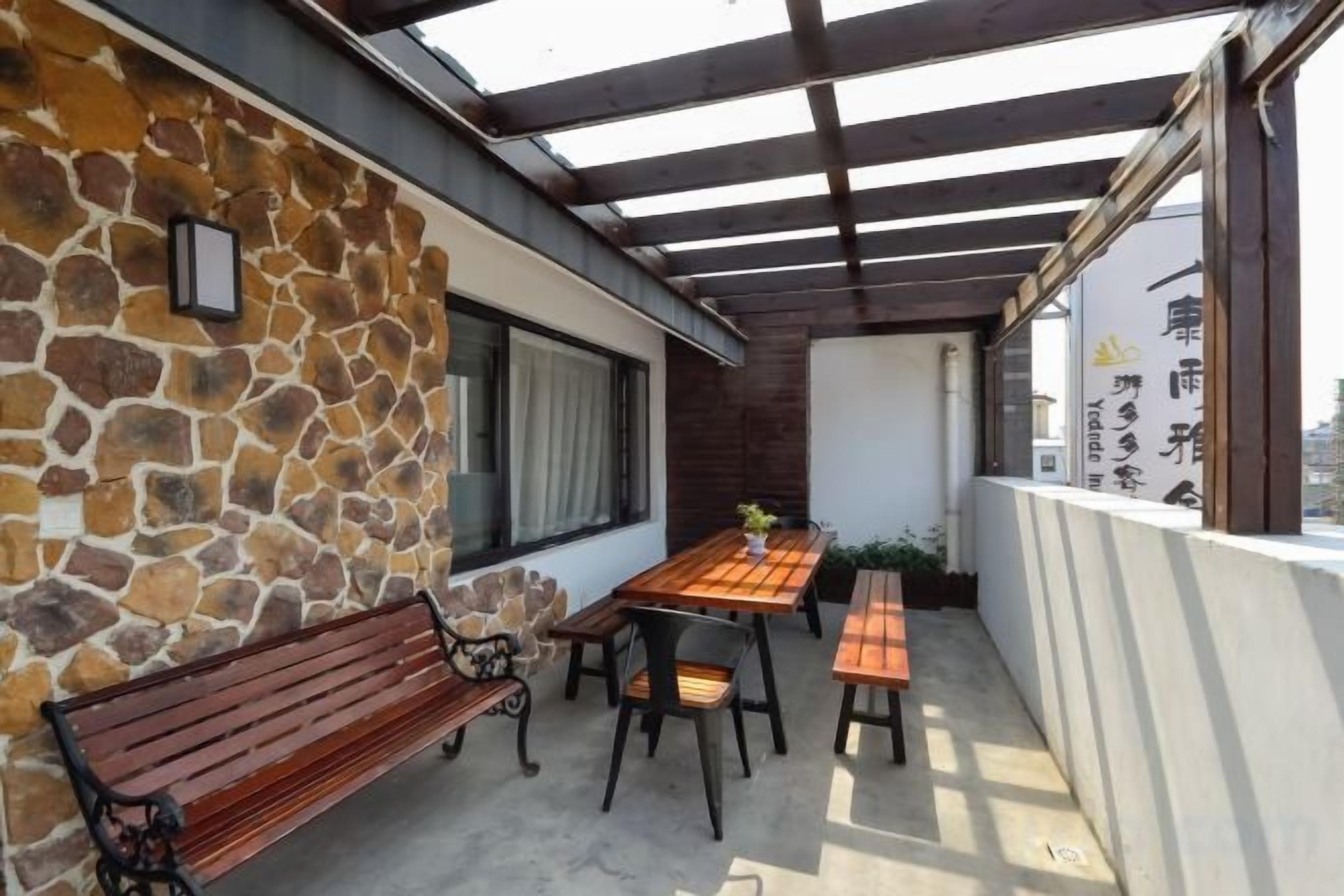 A covered outdoor patio with a stone wall, wooden bench, and table with chairs.