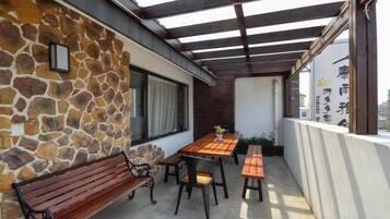 A covered outdoor patio with a stone wall, wooden bench, and table with chairs.