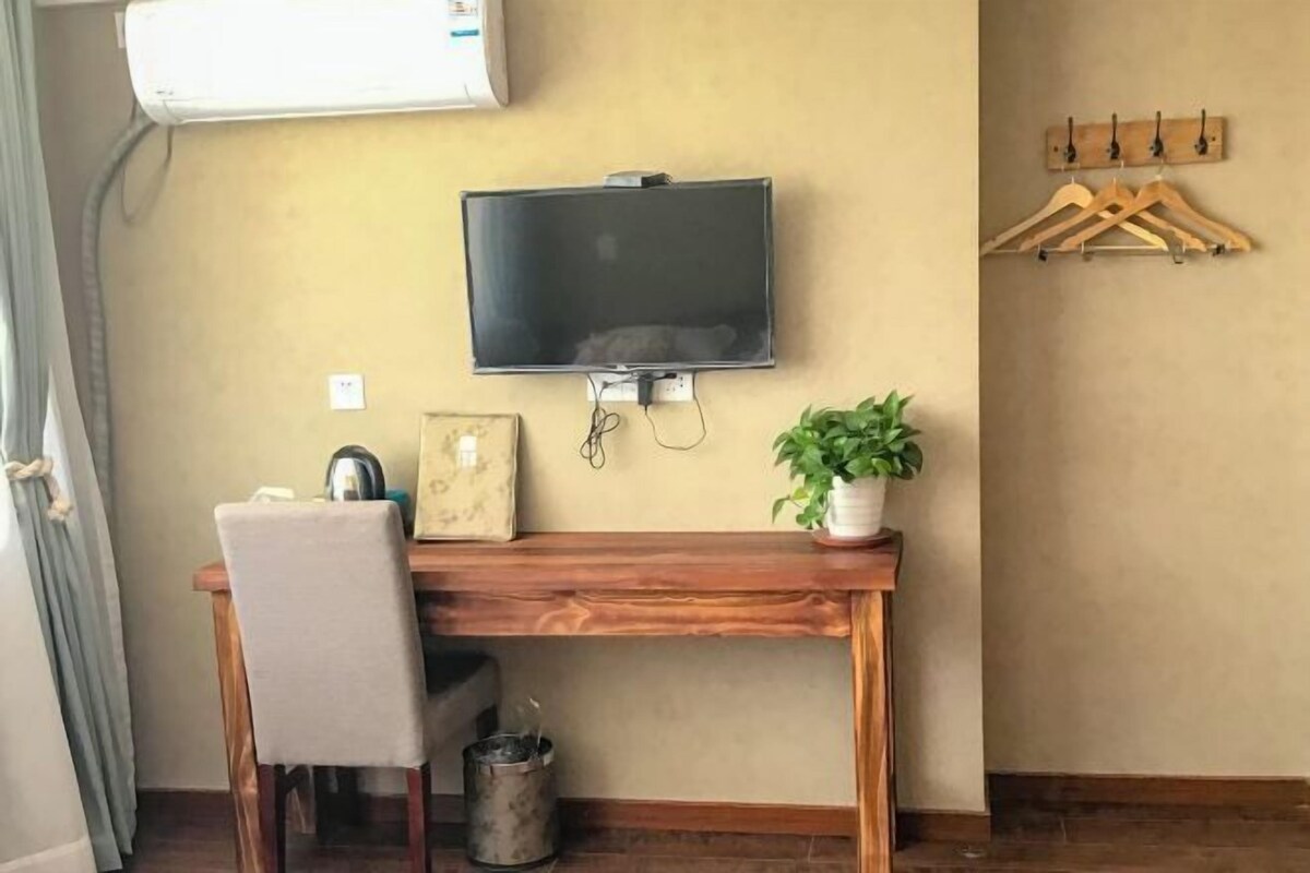 A room with a wooden desk, a television mounted on the wall, a potted plant, and a coat rack with hangers.