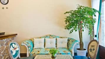 A room with a sofa, a small table, a potted plant, and a clock on the wall.