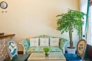 A room with a sofa, a small table, a potted plant, and a clock on the wall. - Nanxun Kangyu Yashe Inn (Huzhou)