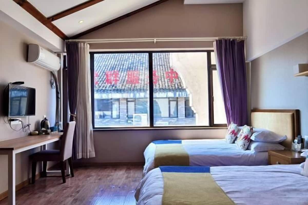 Une chambre d’hôtel équipée d’un bureau, de deux lits, d’une télévision et d’une fenêtre donnant sur un immeuble.