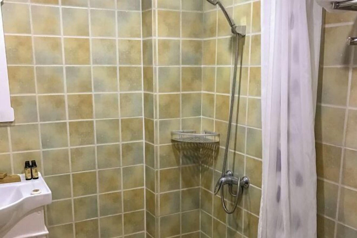 A shower area with a tiled wall, a showerhead, and a shower caddy.