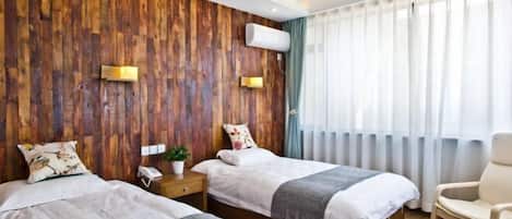 A hotel room with two beds, wooden panel walls, a modern chair, and a large window with curtains.