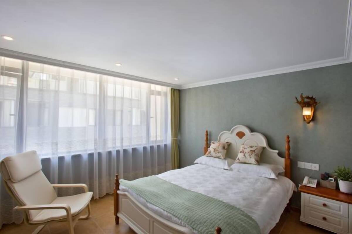 Une chambre à coucher comprenant un lit, une chaise, une table de chevet et un luminaire fixé au mur.