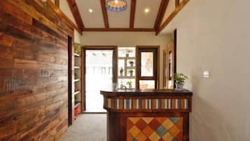 Un pasillo con paredes de madera, una recepción con un estampado geométrico colorido y una puerta que da a una habitación luminosa.