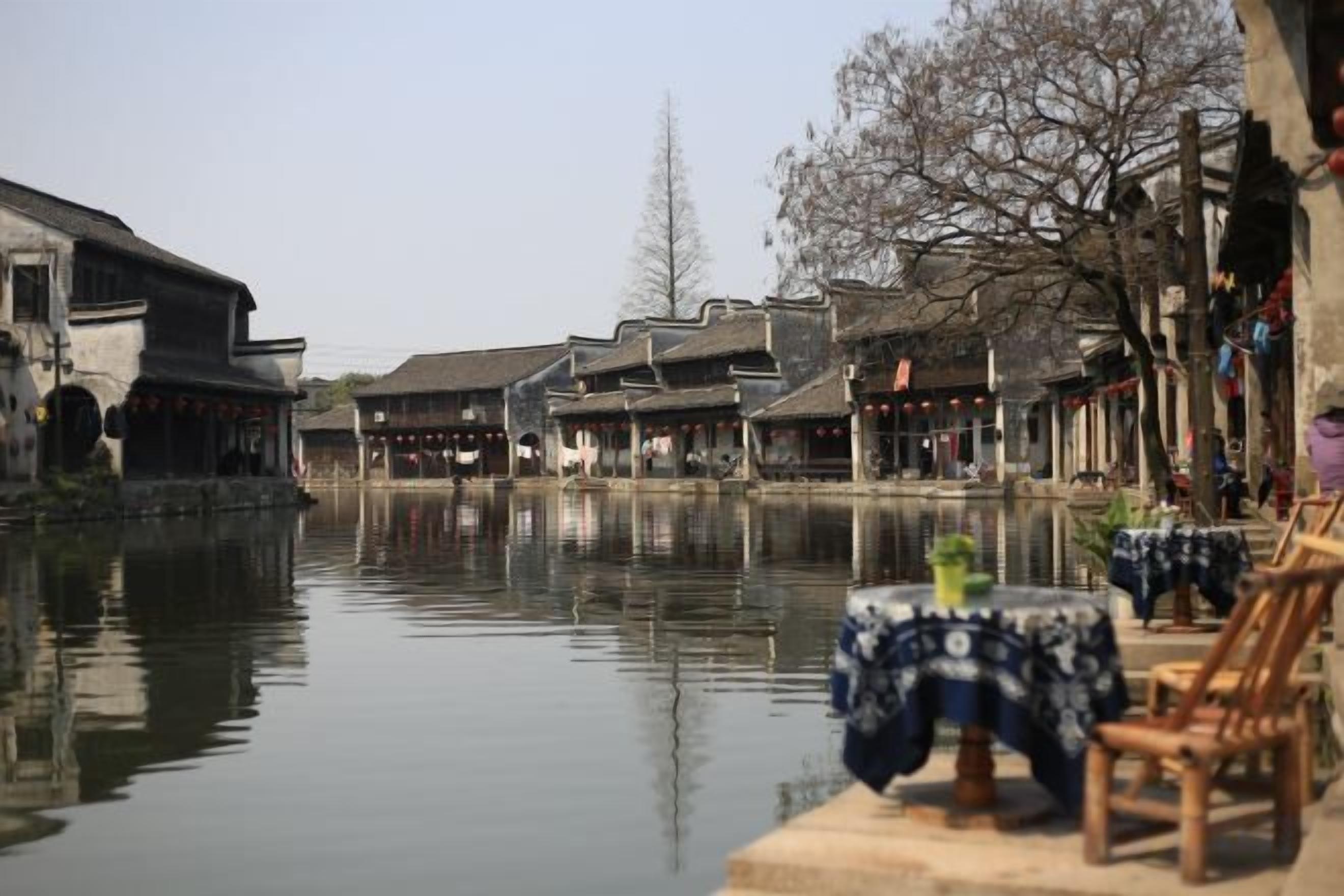 A traditional courtyard with buildings, a calm water body, and a table with a tablecloth.