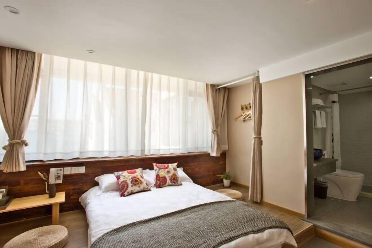 Une chambre moderne avec un grand lit, une table de chevet, une petite plante sur la table de chevet et une vue sur la salle de bain par une porte ouverte.