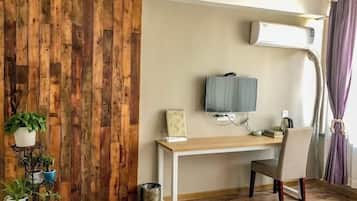 A room with a wooden wall panel, a desk with a chair, a mounted TV, and a window with curtains.