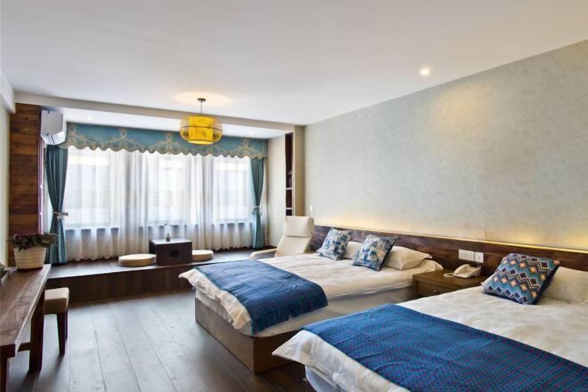 Une chambre d’hôtel avec deux lits, un bureau, une chaise, une fenêtre avec des rideaux et un luminaire suspendu.
