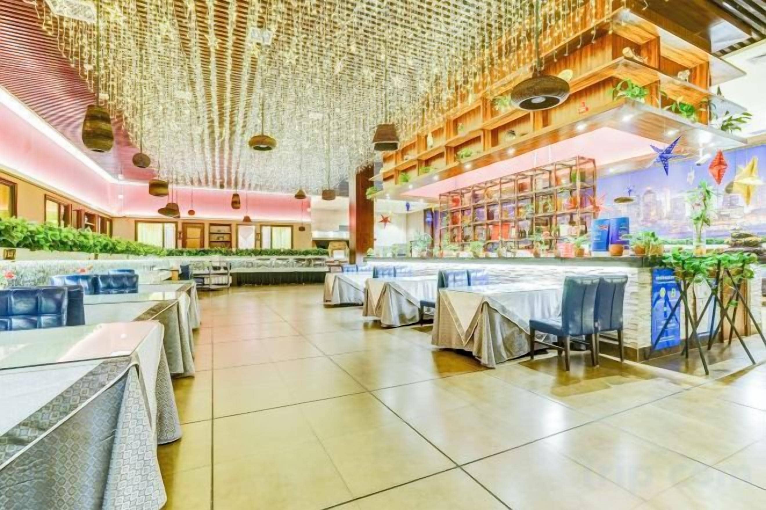 A spacious indoor dining area with multiple tables and chairs, a high ceiling with hanging decorations, and a bar area with shelves.