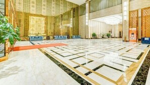 A spacious lobby with a patterned wall, seating area, and a large tiled floor. - Xi Le Hui Hotel (Fujin)