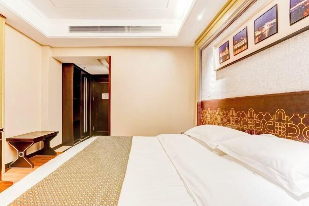 A hotel room with a large bed, a bedside table, a wall-mounted TV, and a door leading to another room.