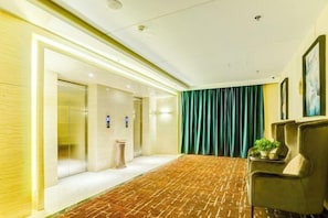 Un vestíbulo de hotel con piso alfombrado, un mostrador de recepción, una cortina verde y un cuadro en la pared.