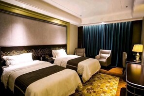 Een hotelkamer met twee bedden, een bureau, een stoel en uitzicht op de stad.