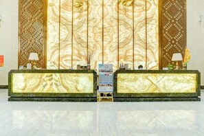 A reception area with marble counters, a decorative wall, and a small table with a lamp. - Xi Le Hui Hotel (Fujin)