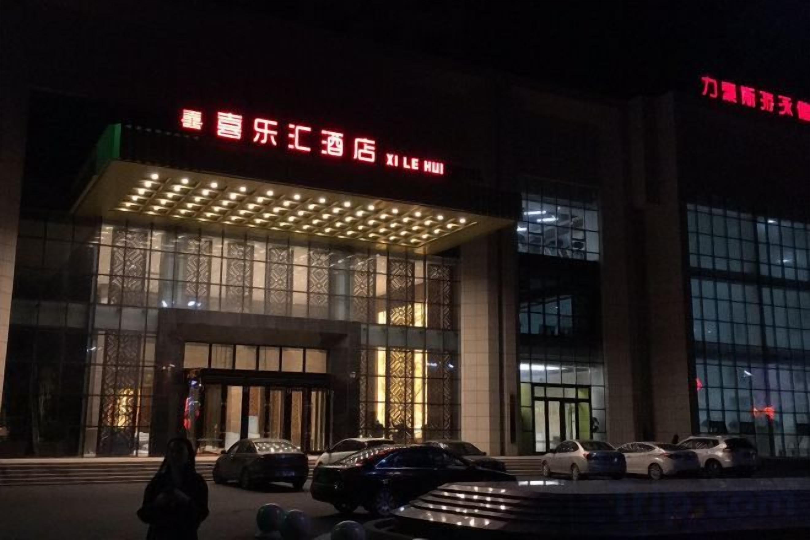 A hotel entrance with illuminated signage, a covered entrance, and cars parked in front.