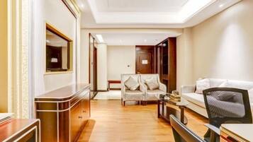 A modern hotel room with a wooden desk, a sofa, and a chair. There is a mirror on the wall and a door leading to another room.