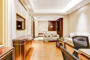 A modern hotel room with a wooden desk, a sofa, and a chair. There is a mirror on the wall and a door leading to another room. - Xi Le Hui Hotel (Fujin)