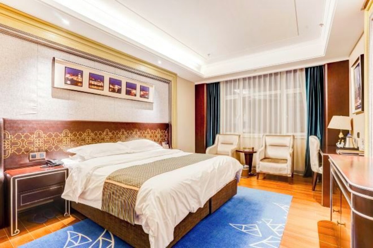 Ein Hotelzimmer mit einem großen Bett, zwei Nachttischen, einem Schreibtisch, einem Sessel und einem Fenster mit Vorhängen.