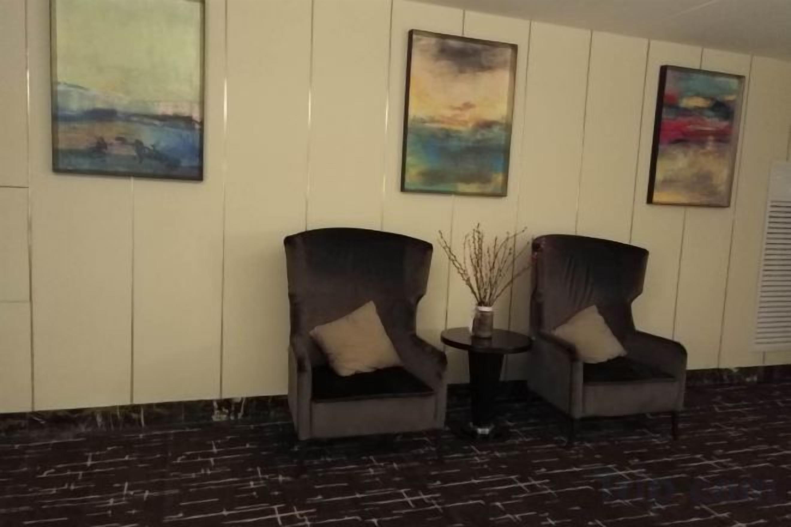 Two armchairs with cushions, a small table with a vase, and three paintings on the wall.