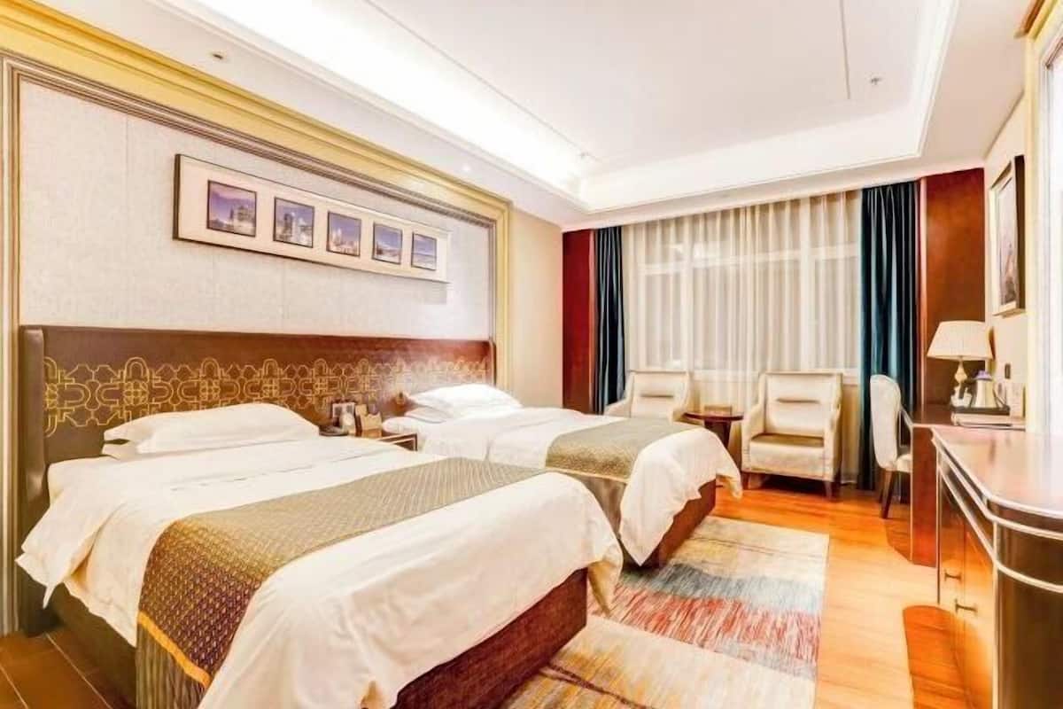 Quarto de hotel com duas camas, uma escrivaninha, uma cadeira e uma televisão.