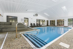Piscina interior com vista clara da área da piscina, escada e área de estar com cadeiras.