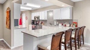 Una cocina moderna con armarios blancos, una isla central con taburetes de bar y un microondas.
