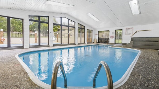 Una piscina interior con paredes de vidrio transparente, suelo de baldosas y zona de cubierta de madera.