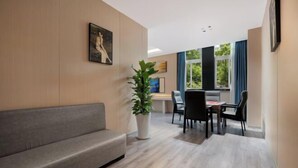 A modern room with a grey sofa, a dining table with chairs, a potted plant, and a painting on the wall. - Shengkai Business Hotel (Chongqing)