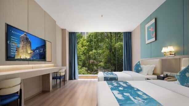 A hotel room with a bed, a desk, a TV, and a view of trees. - Shengkai Business Hotel (Chongqing)