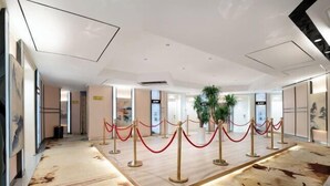 A hotel lobby with a central red rope barrier, a large plant, and a patterned carpet. - Shengkai Business Hotel (Chongqing)
