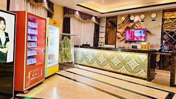 A hotel reception area with a reception desk, vending machines, and a wall-mounted television.