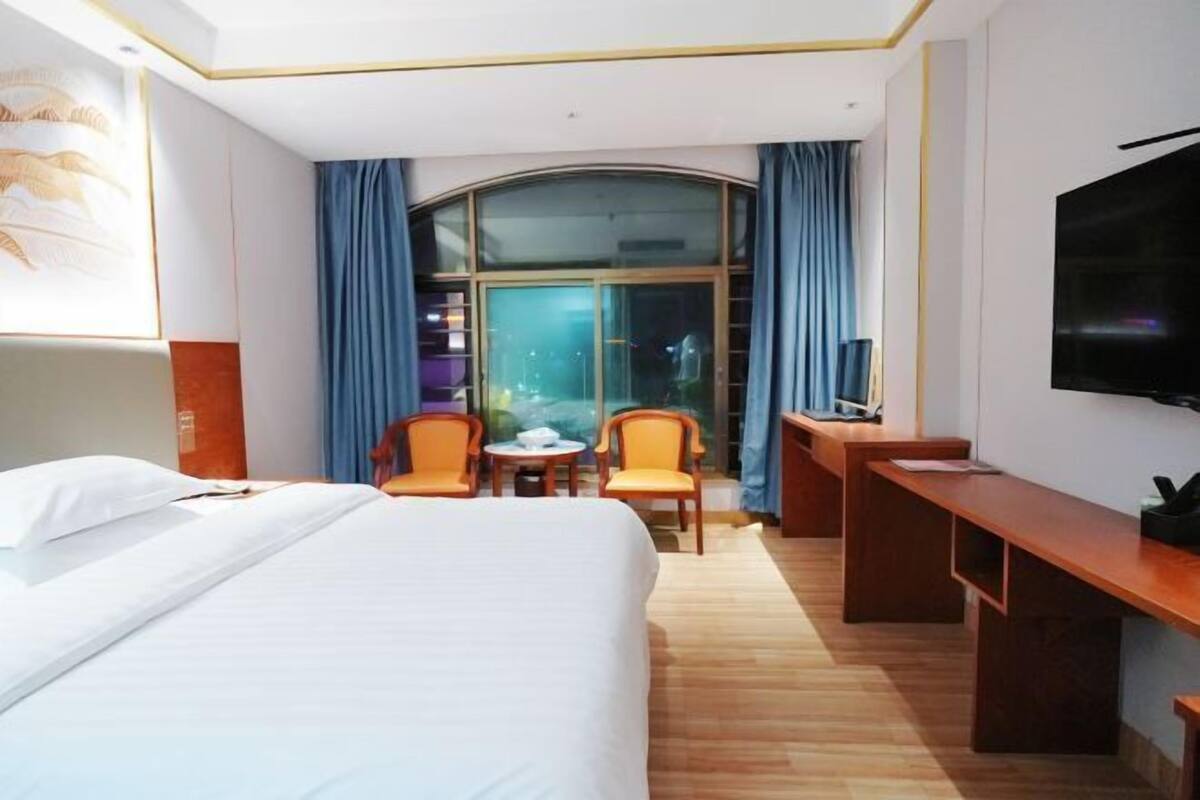 A hotel room with a bed, a desk, a TV, a window with curtains, and a small table with chairs.