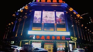 Un hôtel avec une enseigne bien visible, écrite en caractères chinois, de nombreuses fenêtres illuminées et un parking où sont garées plusieurs voitures.