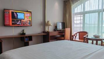 A hotel room with a bed, a desk with a TV, a lamp, and a chair.