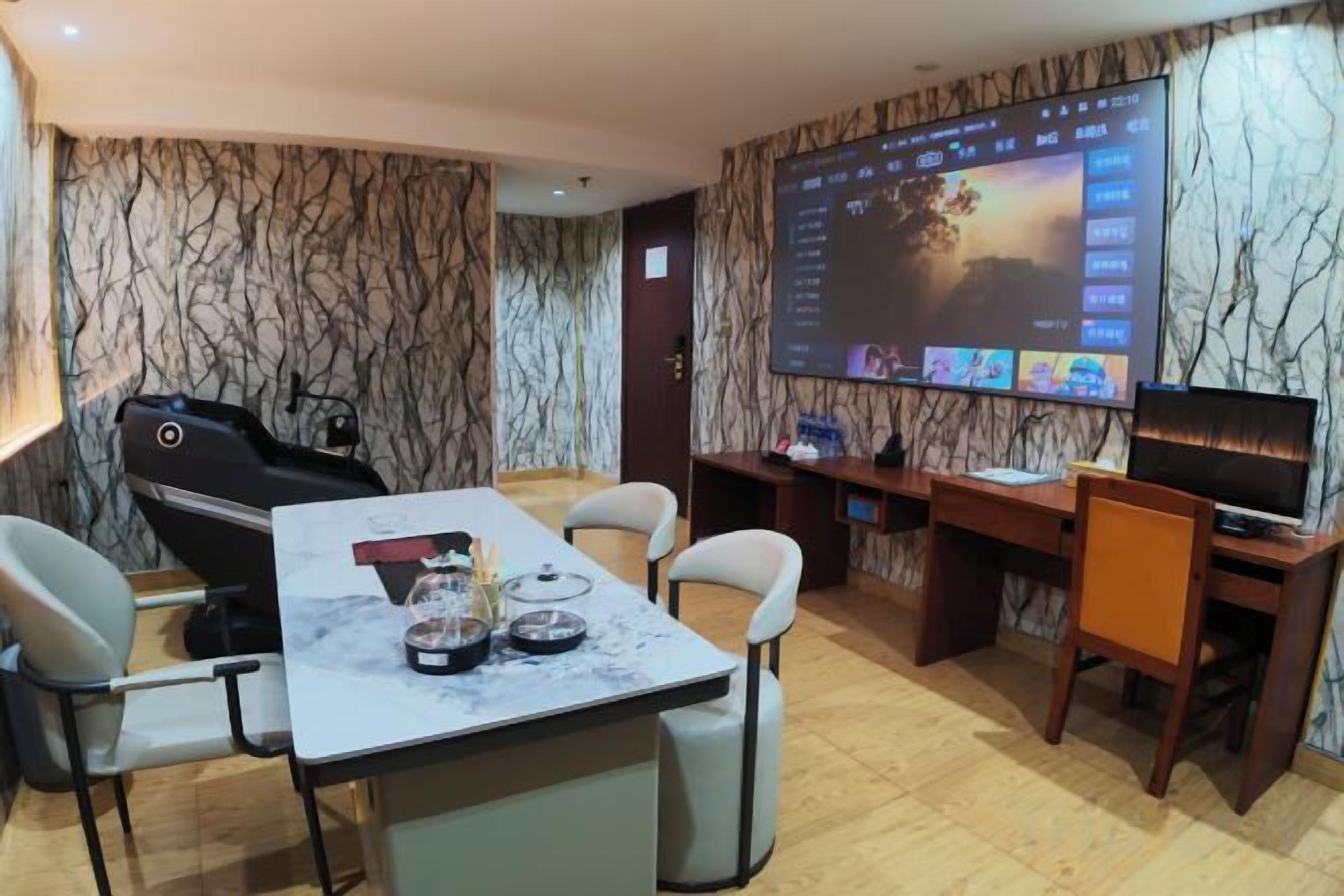 A room with a massage chair, a dining table with chairs, a TV, and a large screen displaying a slideshow.