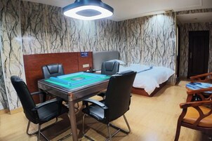 Habitación de hotel con pared de diseño de mármol, cama con cubrecama blanco, mesa de comedor con sillas y lámpara en el techo.
