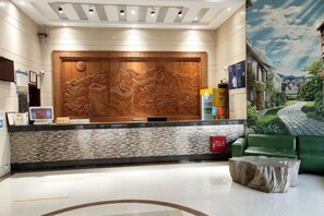 Zona de recepción con un gran panel de madera, un mostrador de recepción, un sofá verde y un mural en la pared.