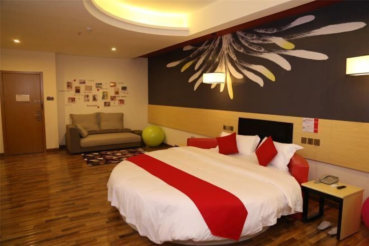 A hotel room with a large bed, a sofa, a wall with photos, and a ceiling light.