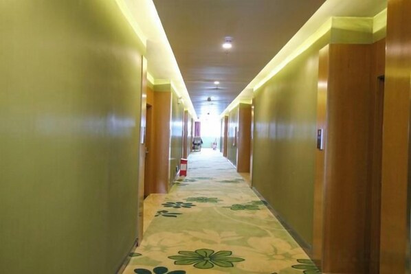 A hotel hallway with carpeted flooring, wooden doors, and overhead lighting.
