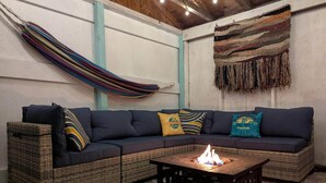Una sala de estar acogedora con un sofá de color oscuro, cojines de colores, una mesita de noche tejida y una chimenea.