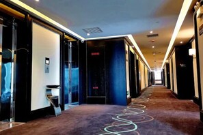 Un pasillo de hotel con puertas de vidrio, suelo alfombrado y una larga galería.