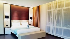 Une chambre d’hôtel moderne, dotée d’un grand lit, d’une table de chevet, d’une lampe de chevet et d’une grande fenêtre avec des rideaux légers.