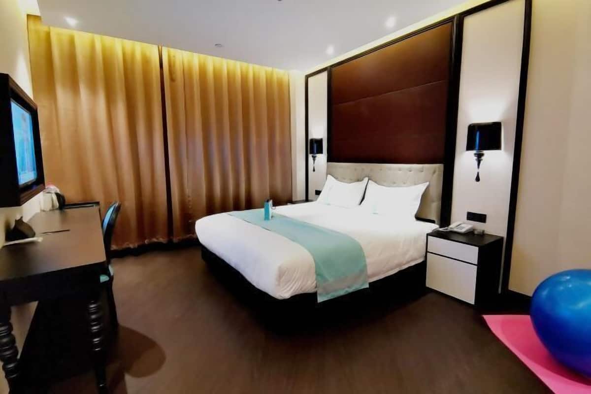 Una habitación de hotel con una cama grande, mesitas de noche, un escritorio y un televisor.