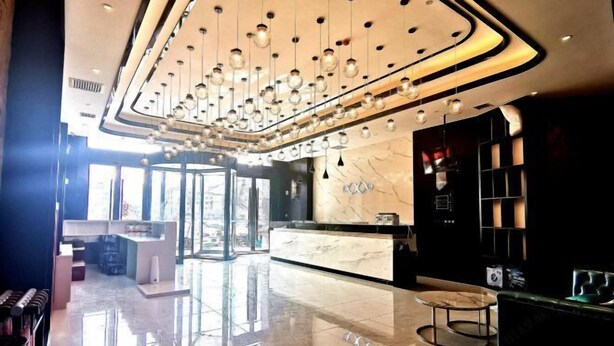 Un hall d’hôtel moderne avec un comptoir d’accueil en marbre, un lustre et un espace salon.